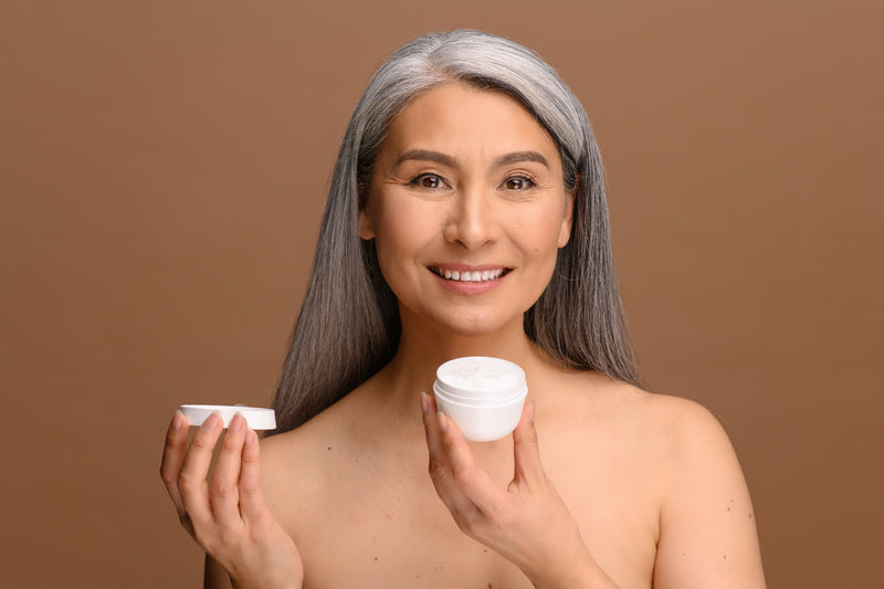 Woman with fresh clean healthy skin stands with jar of moisturizer cream