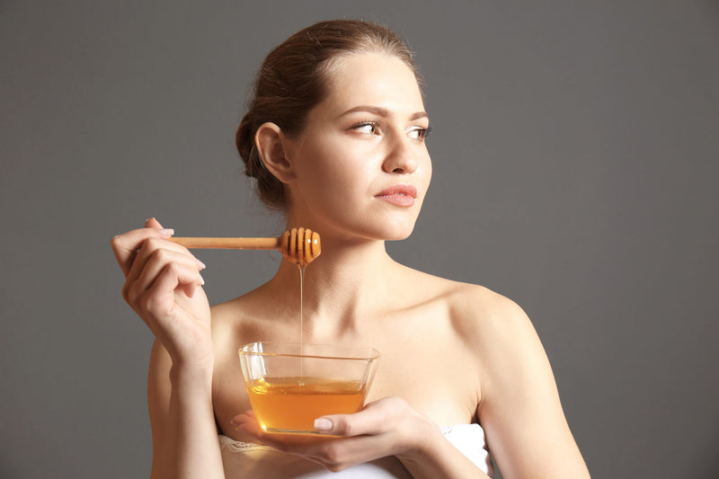Young woman with bowl of honey on grey background