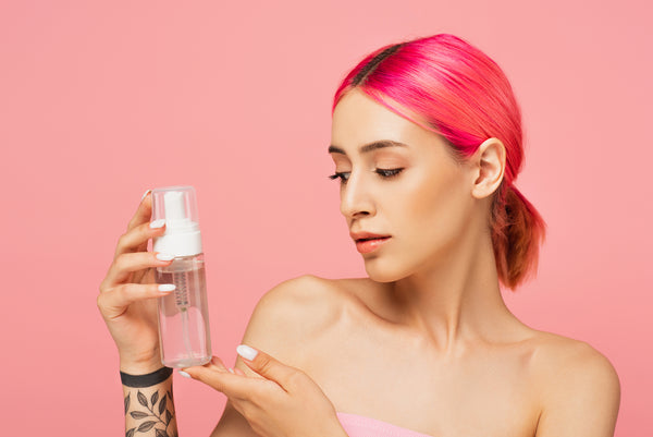 Young woman with red hair looking at bottle with face toner